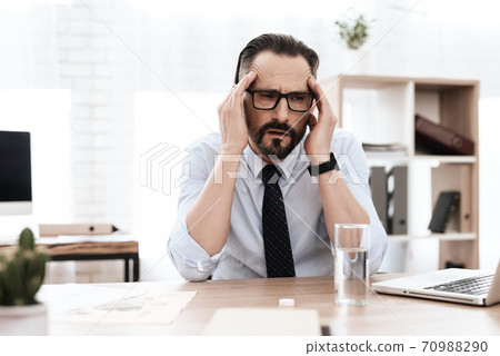 A man with a beard at his desk feels a migraine. A man with a beard at his desk feels a migraine. 70988290