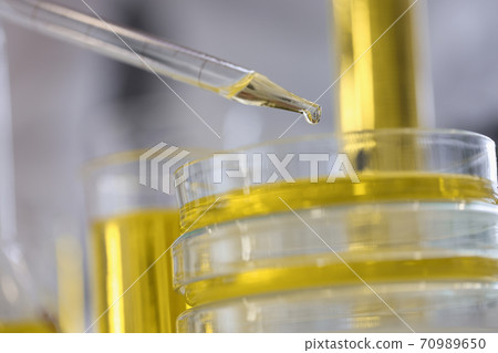Drop of yellow liquid flows out of glass pipette in chemical laboratory closeup 70989650