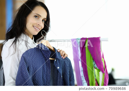 Young woman holds hanger with black shirt in her hands in sewing workshop Young woman holds hanger with black shirt in her hands in sewing workshop 70989686