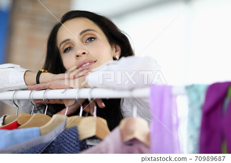 Young brunette woman leaned her hands on rack with hangers in store portrait Young brunette woman leaned her hands on rack with hangers in store portrait 70989687