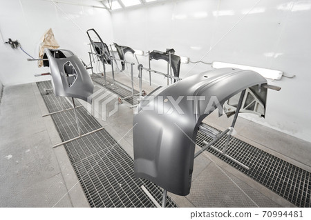 Various parts of the car on the stands for painting. Garage painting car service. Repairing car body work after the accident by working sanding primer before painting. 70994481
