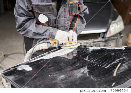 The mechanic works with a grinding tool. Sanding of car elements. Garage painting car service. Repairing car section after the accident. The mechanic works with a grinding tool. Sanding of car elements. Garage painting car service. Repairing car section after the accident. 70994494