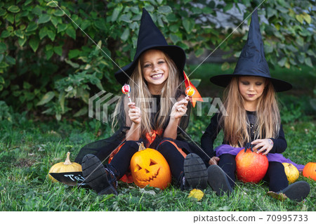 Two funny little girls in witch costumes eating Halloween candy 70995733