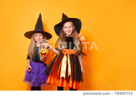 Portrait of two funny little girls dressed up as halloween witch on orange background Portrait of two funny little girls dressed up as halloween witch on orange background 70995755