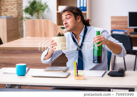 Young male employee drinking alcohol at workplace 70995990