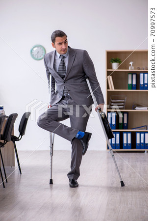 Young leg injured male employee working in the office Young leg injured male employee working in the office 70997573