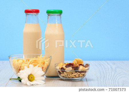 Two bottles of milk with red and green cap and bowls with muesli and cornflakes. 71007373