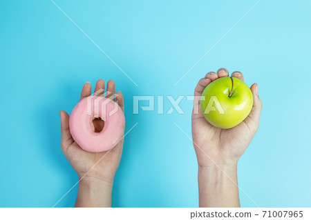 woman holding green apple and pink donut, female choose between fruit is Healthy food and sweet is unhealthy junk foods. Dieting, obesity, eating lifestyle and nutrition concept woman holding green apple and pink donut, female choose between fruit is Healthy food and sweet is unhealthy junk foods. Dieting, obesity, eating lifestyle and nutrition concept 71007965