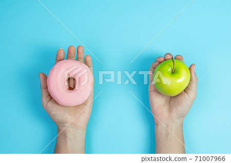 woman holding green apple and pink donut, female choose between fruit is Healthy food and sweet is unhealthy junk foods. Dieting, obesity, eating lifestyle and nutrition concept woman holding green apple and pink donut, female choose between fruit is Healthy food and sweet is unhealthy junk foods. Dieting, obesity, eating lifestyle and nutrition concept 71007966