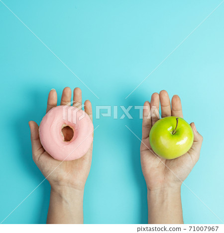 woman holding green apple and pink donut, female choose between fruit is Healthy food and sweet is unhealthy junk foods. Dieting, obesity, eating lifestyle and nutrition concept woman holding green apple and pink donut, female choose between fruit is Healthy food and sweet is unhealthy junk foods. Dieting, obesity, eating lifestyle and nutrition concept 71007967