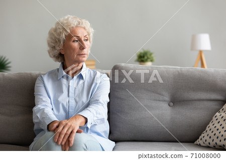 Pensive senior grandma looking away thinking of loneliness on couch 71008000