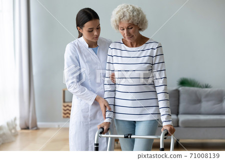 Young woman caregiver helping disabled old grandma patient using walker 71008139