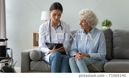 Young female doctor consulting disabled old patient writing in clipboard Young female doctor consulting disabled old patient writing in clipboard 71008140
