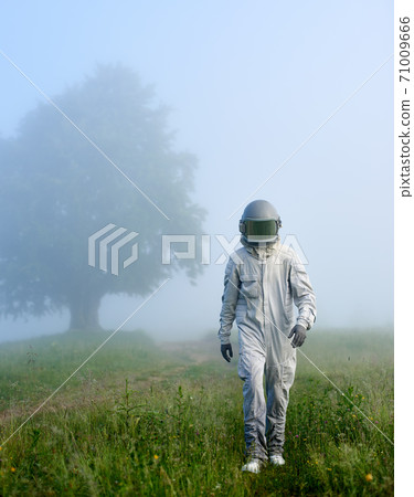 Astronaut walking on grass in foggy valley. Astronaut walking on grass in foggy valley. 71009666
