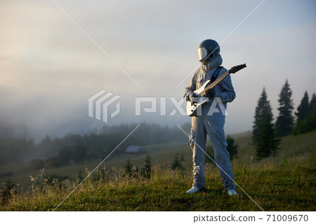 Space traveler standing on grass and holding guitar. 71009670