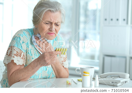 Sad sick senior woman sitting at table Sad sick senior woman sitting at table 71010504