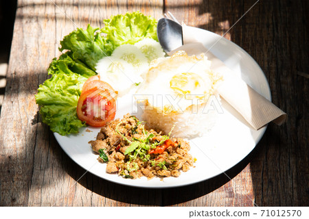 basil stir fry rice with vegetable tomato cucamber salad on white plate and wood table with another food stock photo 71012570