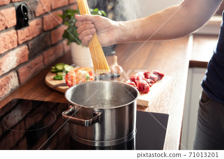 Man's hand throws spaghetti noodles into boiling water Man's hand throws spaghetti noodles into boiling water 71013201
