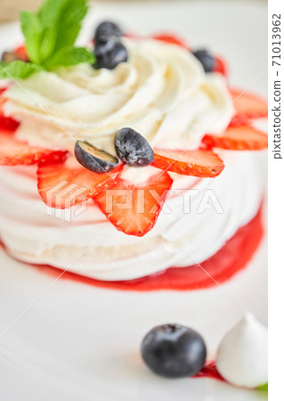Pavlova is a meringue-based dessert with a crisp crust topped. Decorated strawberry, mint leaf, blueberry and whipped cream. Restaurant sweet food 71013962