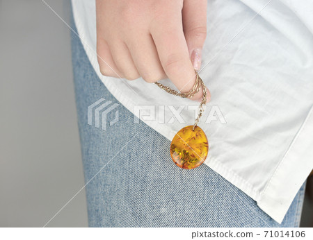 female hand holding a gold chain with amber pendant.  71014106