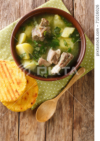 Caldo de costilla is a dish typical of Colombian cuisine it is made mainly from beef ribs with slices of potato, some garlic, onion and cilantro leaves closeup. Vertical top view Caldo de costilla is a dish typical of Colombian cuisine it is made mainly from beef ribs with slices of potato, some garlic, onion and cilantro leaves closeup. Vertical top view 71016026