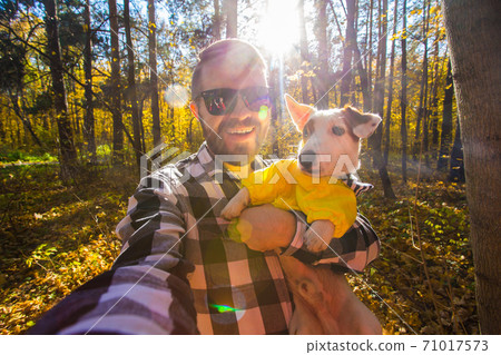 Man taking selfie with his dog at autumn park. Guy posing with jack russell terrier for a picture on the mobile phone outdoors. Pet and people concept. Man taking selfie with his dog at autumn park. Guy posing with jack russell terrier for a picture on the mobile phone outdoors. Pet and people concept. 71017573