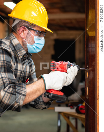 Carpenter at work protects the face with the surgical mask. Covid-19 prevention. Carpenter at work protects the face with the surgical mask. Covid-19 prevention. 71018263