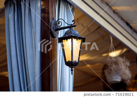 decorative lantern for gazebos and terraces wrought iron, sconces on a brown pillar with blue curtains weighing folds. decorative lantern for gazebos and terraces wrought iron, sconces on a brown pillar with blue curtains weighing folds. 71019021