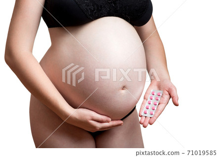 pregnant girl with belly holds in her hand demonstrates sticker with red pills for maternity health, no face on a white background with copy space. 71019585