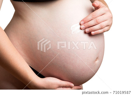 A white cosmetic moisturizer for stretch marks close-up on a white belly is applied to the skin of the pregnant woman belly. 71019587