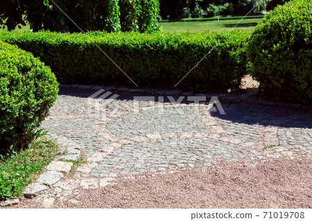 a gravel path that turns into a stone tile path with boxwood fenced with hedges on a sunny day. a gravel path that turns into a stone tile path with boxwood fenced with hedges on a sunny day. 71019708