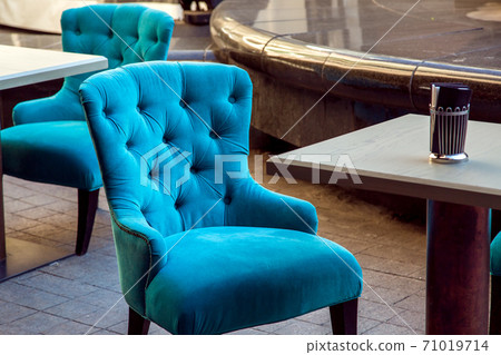 upholstered armchair with fabric covering at the square wooden table on the stone tiles of the street cafe. upholstered armchair with fabric covering at the square wooden table on the stone tiles of the street cafe. 71019714