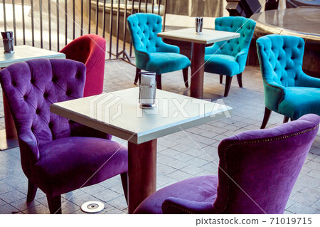 outdoor cafe with square white tables and multi-colored soft textile chairs on the stone paving slabs. outdoor cafe with square white tables and multi-colored soft textile chairs on the stone paving slabs. 71019715
