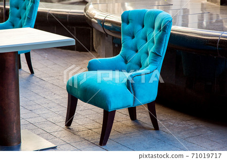 An empty armchair sheathed in soft cloth with a high back in blue is standing on the stone tile of the terrace of the summer cafe. An empty armchair sheathed in soft cloth with a high back in blue is standing on the stone tile of the terrace of the summer cafe. 71019717