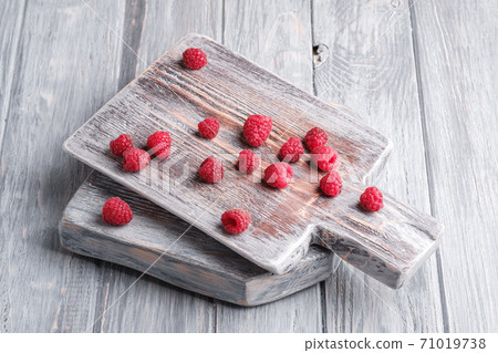 Raspberry fruits on old cutting board, healthy pile of summer berries on grey wooden background, angle view Raspberry fruits on old cutting board, healthy pile of summer berries on grey wooden background, angle view 71019738