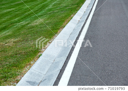 Street gutter of a stormwater drainage system on the side of an road with markings and grass. 71019793