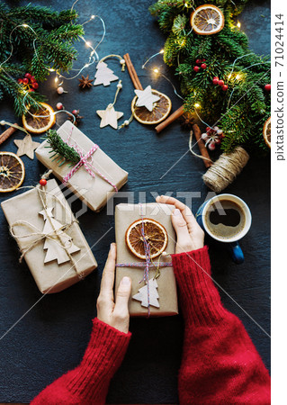 Top view of female hands in a red cozy sweater holding a decorated gift Top view of female hands in a red cozy sweater holding a decorated gift 71024414