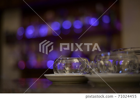 Glass round utensils candlesticks on white saucers, made. Against the background of the purple lights of the bar. Glass round utensils candlesticks on white saucers, made. Against the background of the purple lights of the bar. 71024455