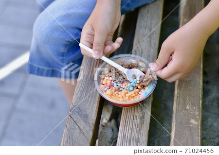 Children hands with a spoon, for eating mini small multicolored ice balls of fruit and chocolate ice cream.  71024456