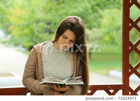A young girl with long hair reads a book in the Park. A young girl with long hair reads a book in the Park. 71024971