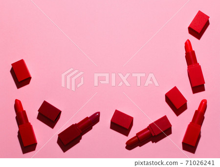 A group of bright red lipsticks is spread on a pastel pink background. A group of bright red lipsticks is spread on a pastel pink background. 71026241