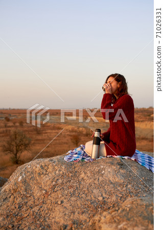 Young woman in sweater relaxing, drinking coffee and enjoying sunset in autumn. 71026331
