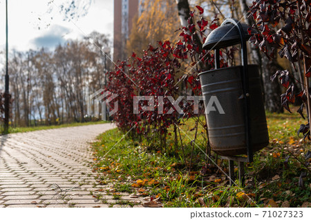 Trash bin in a city park, trash bin made of metal in green grass in open nature near a road made of stones, in the afternoon in sunny weather concept of webinar activity Trash bin in a city park, trash bin made of metal in green grass in open nature near a road made of stones, in the afternoon in sunny weather concept of webinar activity 71027323