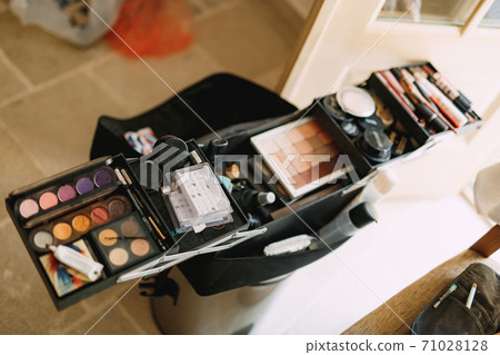 Makeup artist set. Large open cosmetic bag with eyeshadow, blush and lipstick in a bright room. Makeup artist set. Large open cosmetic bag with eyeshadow, blush and lipstick in a bright room. 71028128