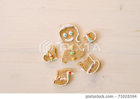 Gingerbread man with severed legs and arms. The limbs of the cookie are separated from the body. Christmas gingerbread on a white wooden background. 71028394