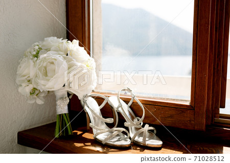White sandals of the bride on the windowsill with a bouquet of roses on a wooden windowsill by the window overlooking the mountains. 71028512
