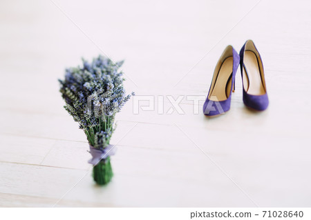 A bouquet of lavender and women's purple high-heeled shoes on a white wooden texture. A bouquet of lavender and women's purple high-heeled shoes on a white wooden texture. 71028640