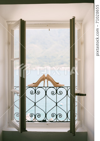 Bride's shoes on a metal lattice in an open window against the background of the sea. 71028655