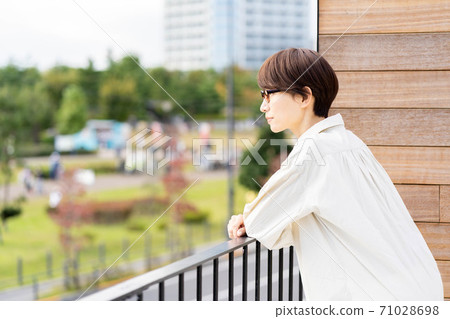 Woman looking out at the lush park from the balcony Woman looking out at the lush park from the balcony 71028698