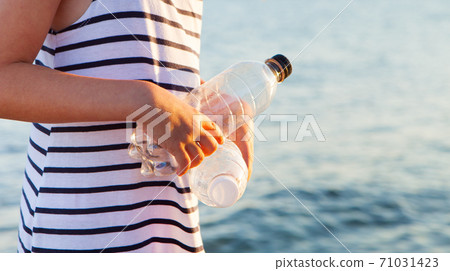 Young girl cleans beach, gathering plastic bottles. Close up. 71031423